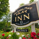 A sign for The James Place Inn displays the address 11 Holbrook Street and indicates vacancy amid flowers.