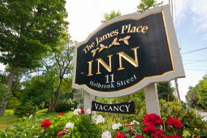 A sign for The James Place Inn displays the address 11 Holbrook Street and indicates vacancy amid flowers.
