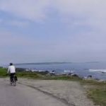 Two people ride bicycles on a paved road beside the ocean—one of the best things to do in Maine.
