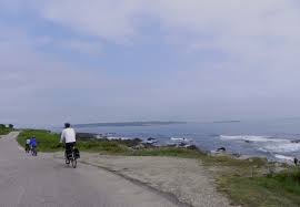 Two people ride bicycles on a paved road beside the ocean—one of the best things to do in Maine.