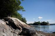 Rocky shoreline with boulders and trees—perfect for vacationing in Maine under a clear blue sky.