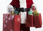 A person dressed as Santa Claus holds red shopping bags and gifts—ready for the best Christmas shopping in Maine.