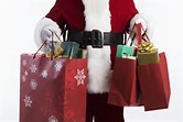 A person dressed as Santa Claus holds red shopping bags and gifts—ready for the best Christmas shopping in Maine.