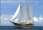 A white sailboat with two masts sails on calm blue water—classic scenery for a Maine vacation.