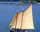 A two-masted sailboat with tan sails glides near shore—a classic scene among the best things to do in Maine.