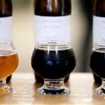 Three beer glasses sit by labeled bottles—a cozy scene after a day exploring things to do in Freeport Maine.