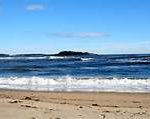 A sandy beach with gentle waves and a distant island—one of the best things to do in Freeport, Maine under a clear sky.