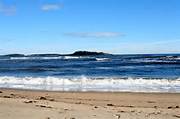 A sandy beach with gentle waves and a distant island—one of the best things to do in Freeport, Maine under a clear sky.