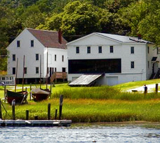 Two white buildings and wooden boats line a grassy shore—classic scenes of vacationing in Maine.