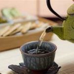 A green teapot pours tea into a ceramic cup at Bhavana spa, with snacks set on the table in the background.