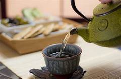 A green teapot pours tea into a ceramic cup at Bhavana spa, with snacks set on the table in the background.