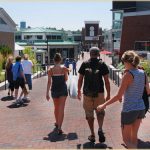 People stroll a sunny shopping area near the clock tower—perfect for itineraries for your James Place Inn vacation in Freeport.